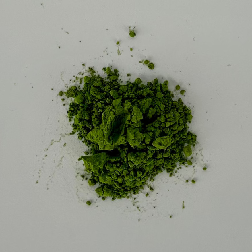 A small pile of bright green matcha powder, scattered on a plain light gray background.
